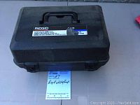 Closed black hard plastic carrying case for Rigid utility pump with model label and handle visible