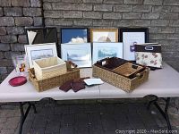 Full lot overview showing prints, frames, baskets, and decorative items on table against brick wall