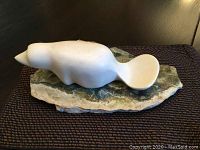 White soapstone beaver carving from side view, showing smooth rounded form and multicolored stone base