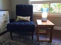 Front view of blue tufted chair with silk cushion next to nesting tables