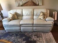 Front view of pale blue leather sofa with two gold paisley pillows
