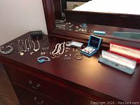 Wide view of assorted costume jewellery including necklaces, bracelets, earrings, and rings on a wooden dresser beneath a mirror