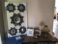 Photo showing the set of 5 starburst mirrors still in original packaging, dark blue fabric table runner folded, silk runner partially visible, two photo holders, small lamp with beige shade, and some small decor items on a wooden surface against a wall.