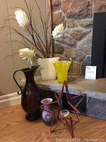 Photo of various home accent pieces including ceramic vases, artificial flowers, and metal star-shaped decor on and around a stone fireplace hearth.