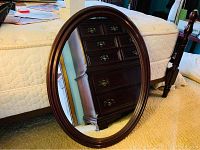 Front view of oval mirror leaning against bed, showing full shape and reflection