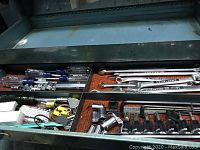 Top inside view of open metal toolbox showing socket sets, wrenches, screwdrivers, and other tools organized in the tray.