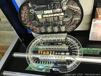 Open clear plastic organizer case showing sanding drums, grinding stones, polishing wheels and mandrels