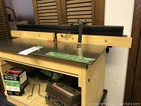 Overall view of custom router table assembly with metal top, fence, and plywood box housing the router.
