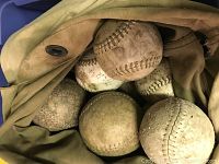 Six used softballs inside a canvas duffel bag.