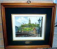 Framed oil painting showing a view of Chateau De Ramezay with green roofs and a street lamp, signed by artist.