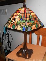 Front view of stained glass table lamp, showing vibrant floral pattern of colored glass pieces and bronze-colored metal base.