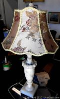 Full view of antique alabaster table lamp showing carved alabaster body and square base with floral patterned, scalloped damask fabric shade trimmed in yellow braid.