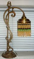 Front angled view of the brass-tone metal lamp stand with hanging beaded shade showing detail of the curved design and bead fringe.
