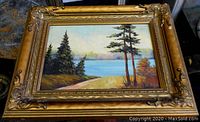 Front view of oil painting depicting a tranquil landscape with pine trees and water, signed J. Hunter, in an ornate gilt wood frame.