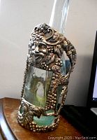 Side view of Art Nouveau silver plated Bacchus satyr head wine caddy bottle holder with embedded glass bottle, showing grapevine and leaf designs.