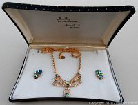 Full set of goldtone iridescent rhinestone necklace and matching earrings displayed inside white lined black fitted jewelry box with brand and series name stamped on inner lid.