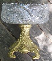 Side angle showing crystal bowl with intricate star and swirl cut pattern set on ornate gold metal pedestal base with scroll and floral details.