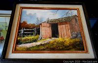 Framed mid-century oil painting on board showing rustic cabin with open door and fence in woods scene. Close-up view includes frame details and artist signature.