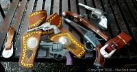 Full view of 5 toy guns and 2 leather belts and holsters laid on metal surface