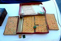 Photo showing the Mahjong tiles arranged on boards with orange Bakelite bottoms visible, the open box, instruction booklet, and a small plastic bag with markers or counters.