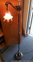 Full view of the Gothic style floor lamp showing the two-tone metal base, pole, and arm with the lily-shaped art glass shade lit.