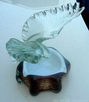 Clear glass eagle sculpture with outspread wings mounted on a brown and white mottled glass bowl base. Side view showing wing detail and base color variation.