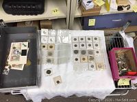 Tray of assorted coins displayed on cloth, including cardboard flips, plastic pages and loose coins in a box