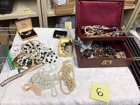 Overview of the jewelry lot on a white cloth, showing multiple necklaces, a bracelet, and jewelry box containing more pieces.