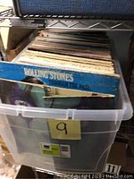 Plastic storage bin containing a stack of vinyl LP albums including a visible Rolling Stones album
