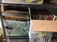 Two boxes filled with vinyl records on a metal shelf, viewed from above.