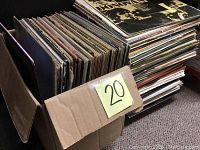 Large cardboard box packed with a variety of vinyl records, showing quantity and general condition.