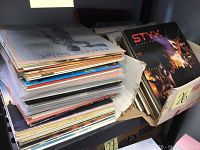 Two cardboard boxes filled with vinyl LP records, one box shows a Styx album at front