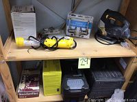 Shelf with assorted tools and hardware including yellow cordless tool, Milwaukee drill, tool boxes, hardware packs, and Gatehouse door handle set.