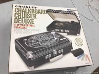 Box of Crosley Chalkboard Cruiser Deluxe 3-speed portable turntable showing branding and design features.