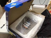 Open box of the white plastic electronic pet door showing the main product wrapped in plastic on a table.