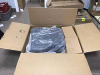 Open cardboard box containing seat and backrest cushions wrapped in plastic and foam inserts