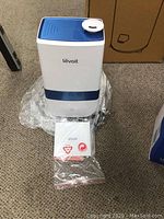 Levoit LV450CH humidifier shown on plastic wrap with user manual placed in front, white and blue rectangular humidifier with mist nozzle on top.