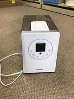Front view of the Loevoit LV600HH humidifier showing display, buttons, and power cord on a carpeted floor.