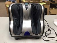 Front view of foot massager showing dual compartments, silver housing and black foot sleeves, cord visible