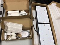 Open cardboard box containing two white driver units, cables and styrofoam packing.