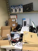 Photo showing multiple boxed laptop chargers and cables on shelf, plus boxed items in original packaging.