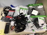 Image of assorted cables, adapters, remote control, and packaged computer accessories on a white surface.