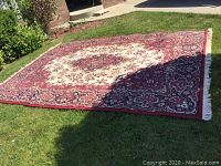Full view of the large gold and burgundy Oriental area rug on grass, showing overall pattern and size.