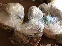 Six large clear plastic bags filled with assorted bed linens, including comforters, blankets, and sheets, placed on chairs and floor
