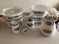 Complete 14 piece CorningWare set with casseroles, lids, coffee pot, cream pitcher, sugar and pepper shakers arranged on a table.