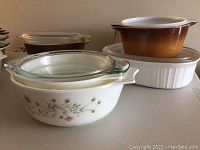 Multiple Pyrex casserole dishes with lids featuring floral patterns and a white casserole dish with small orange flower design.