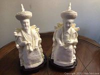 Two white oriental-style figurine sculptures on a wooden surface, showing full front view and detail of both pieces.