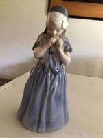 Front view of Royal Copenhagen porcelain figurine showing the girl in a blue dress and bonnet.