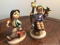 Two Hummel figurines on a wooden surface, showing both items in the lot.