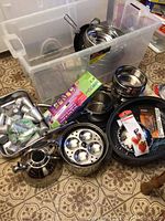 Clear plastic storage bin with various cookware items grouped around it on floor.